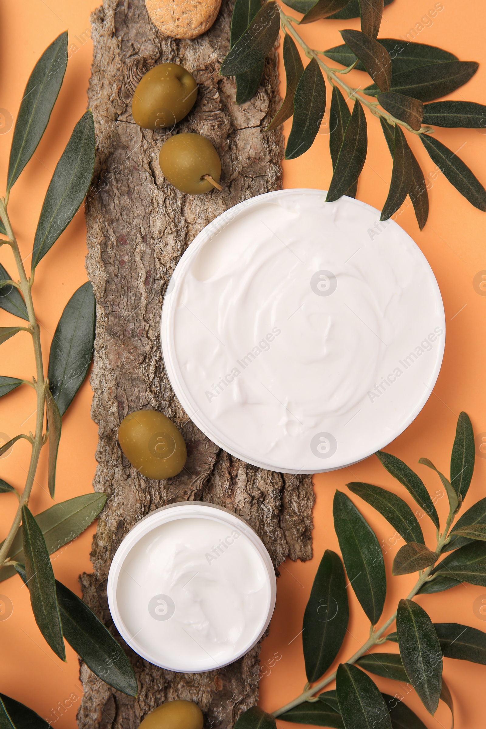 Photo of Flat lay composition with jars of cream and olives on pale orange background