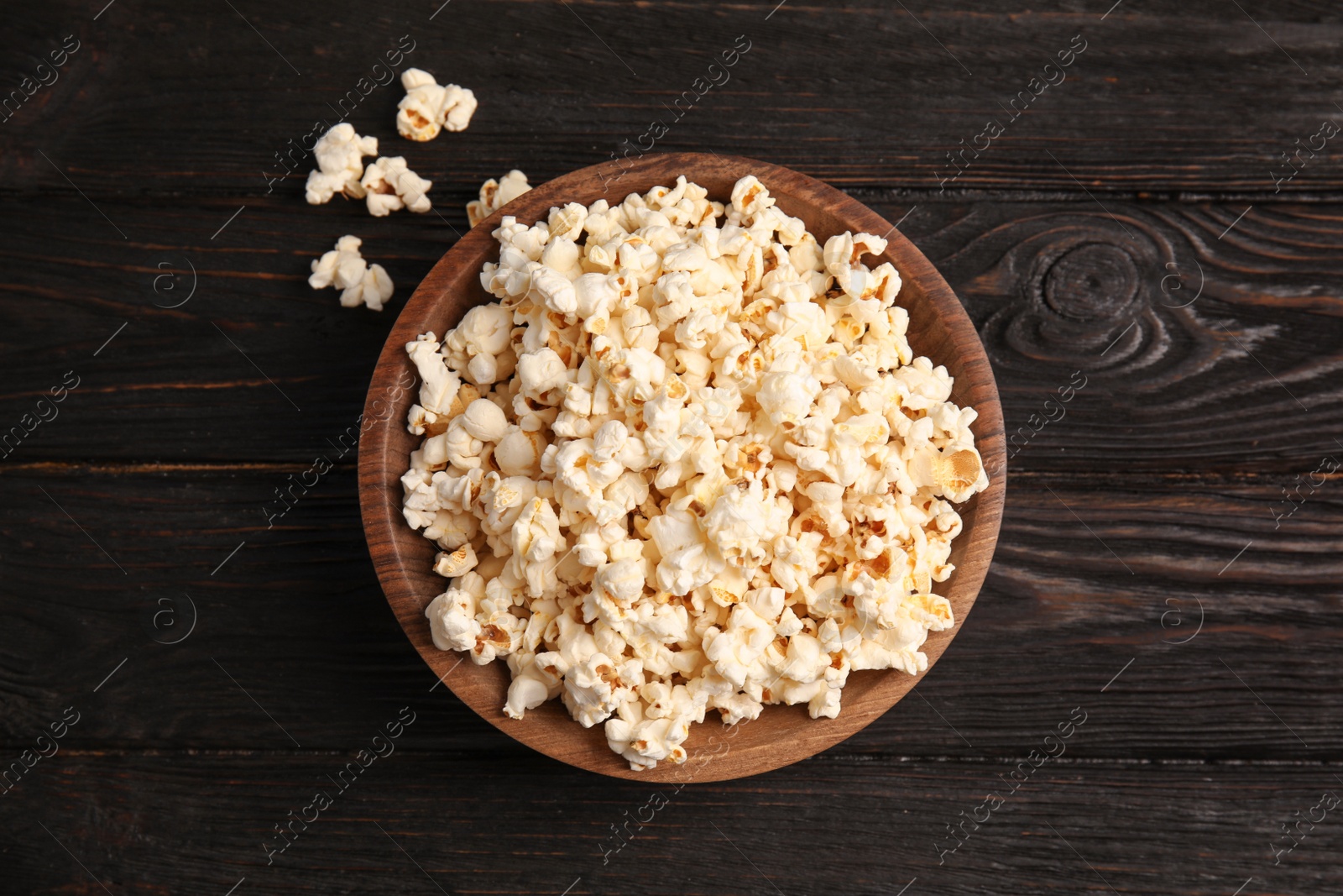 Photo of Bowl of tasty popcorn on wooden background, top view