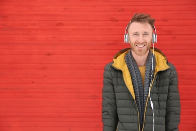 Photo of Young man listening to music with headphones against color wall. Space for text