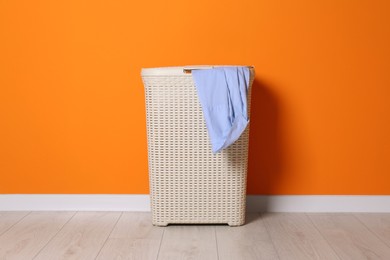 Laundry basket with clothes near orange wall indoors