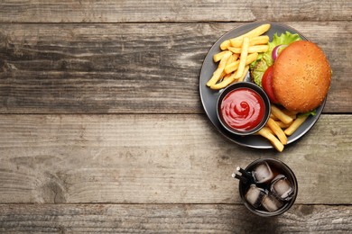 French fries, tasty burger, sauce and drink on wooden table, flat lay. Space for text