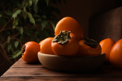 Photo of Delicious ripe persimmons in bowl on wooden table, space for text