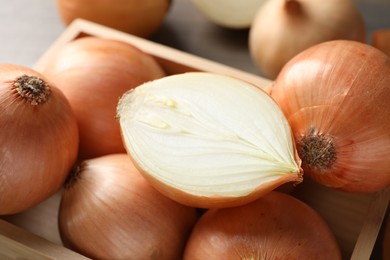 Photo of Whole and cut onions in wooden box, closeup