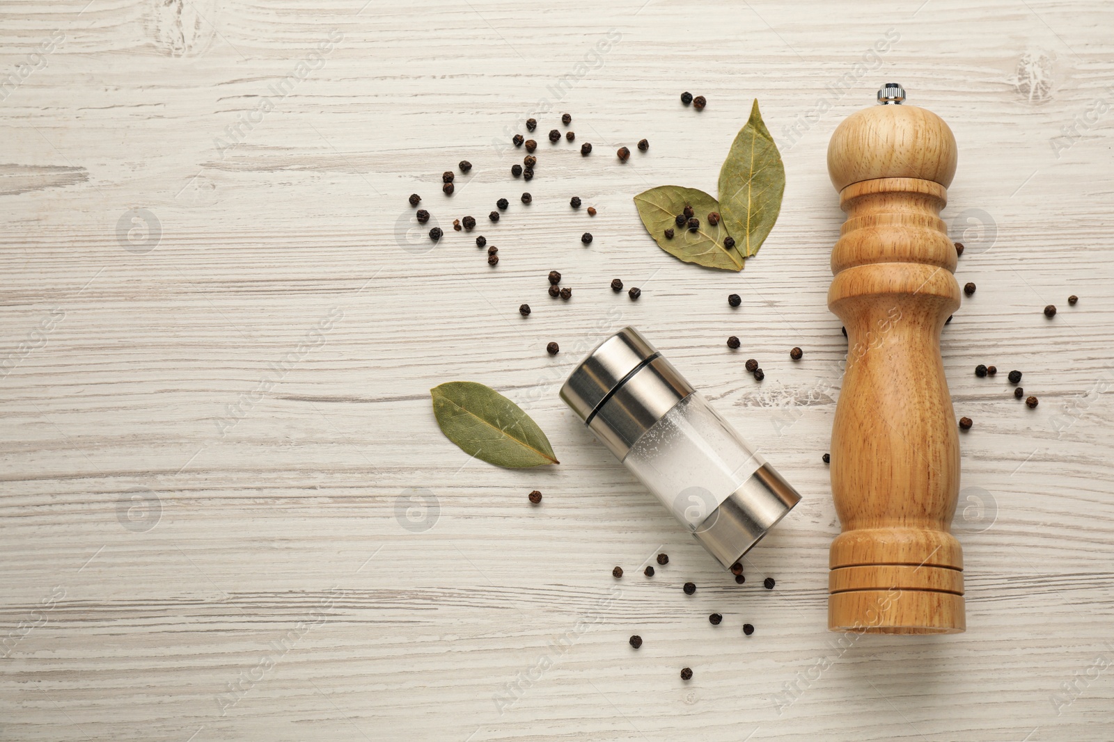 Photo of Salt and pepper shakers with bay leaves on white wooden table, flat lay. Space for text