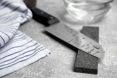 Sharpening stone and knife on grey table, closeup