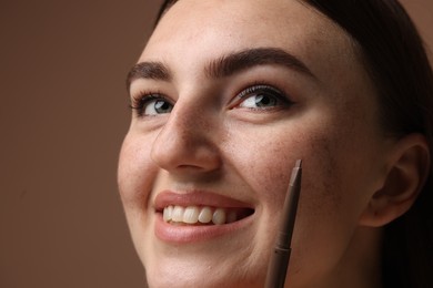 Photo of Smiling woman with freckle pen on brown background, closeup