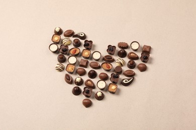 Heart made with delicious chocolate candies on beige background, above view