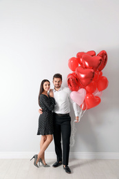 Photo of Happy young couple with heart shaped balloons near light wall. Valentine's day celebration