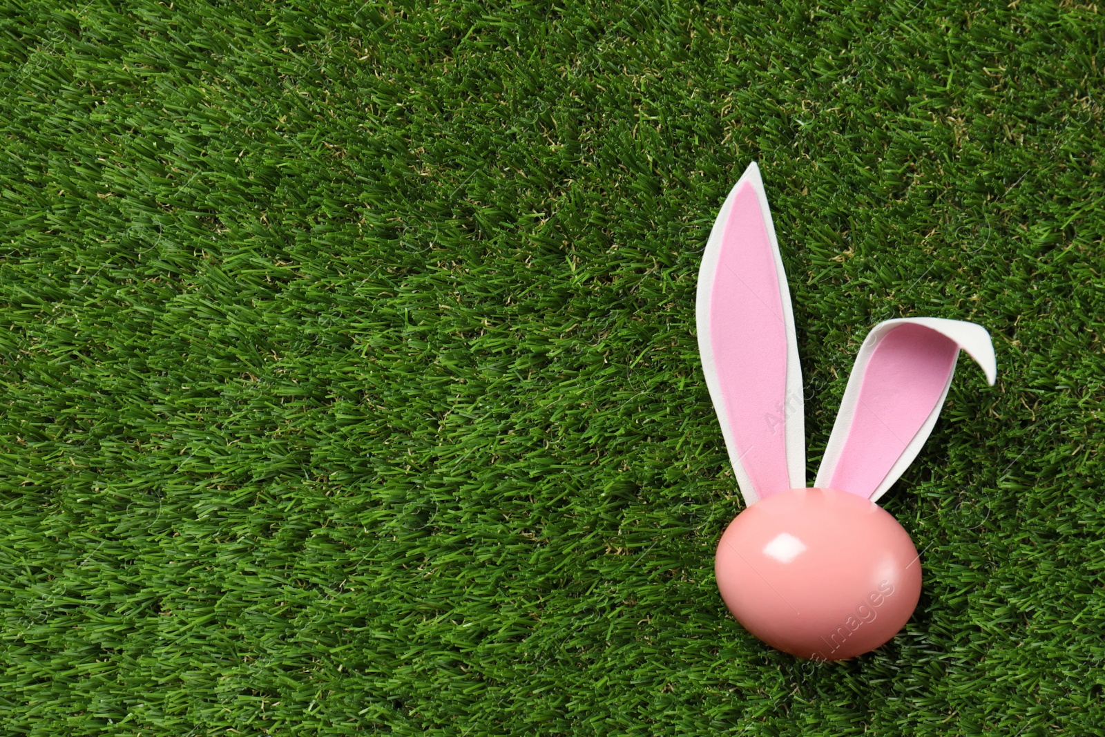 Photo of Flat lay composition of funny Easter bunny ears and dyed egg on green grass, space for text