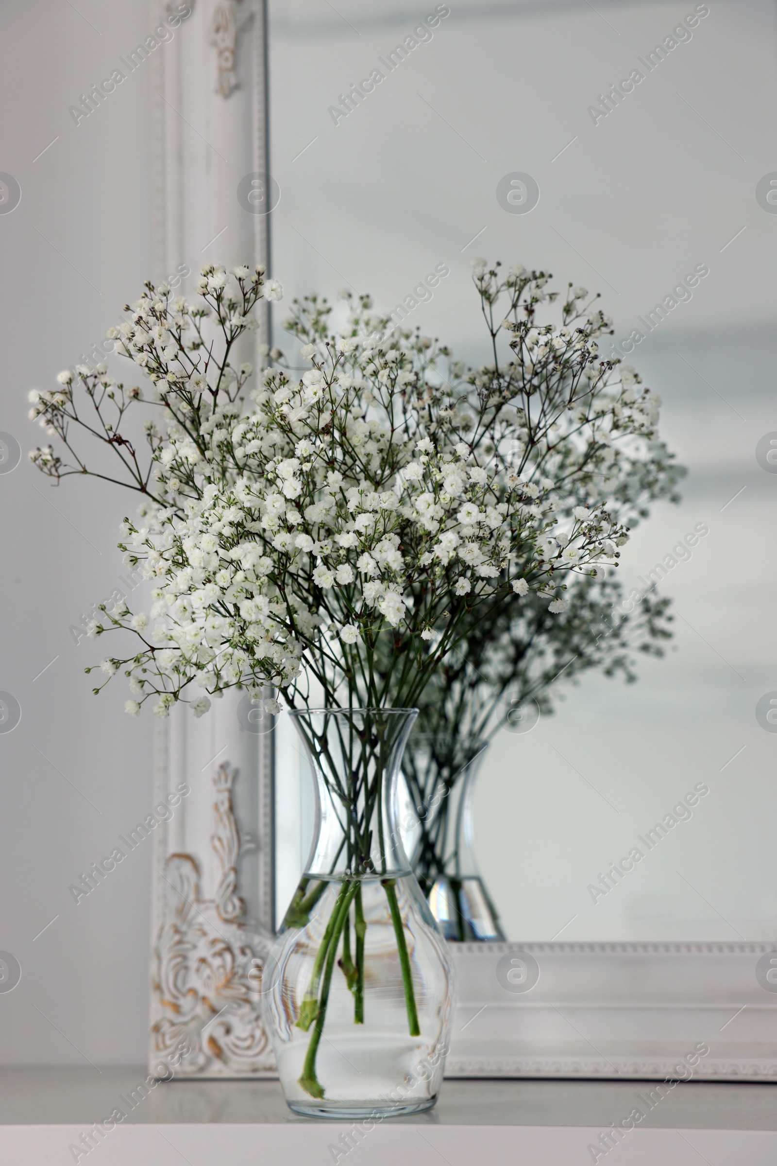 Photo of Beautiful gypsophila flowers in glass vase on white table near mirror indoors