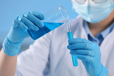 Photo of Scientist working with beaker and test tube on light blue background, closeup