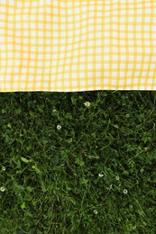 Photo of Checkered picnic tablecloth on fresh green grass, top view. Space for text