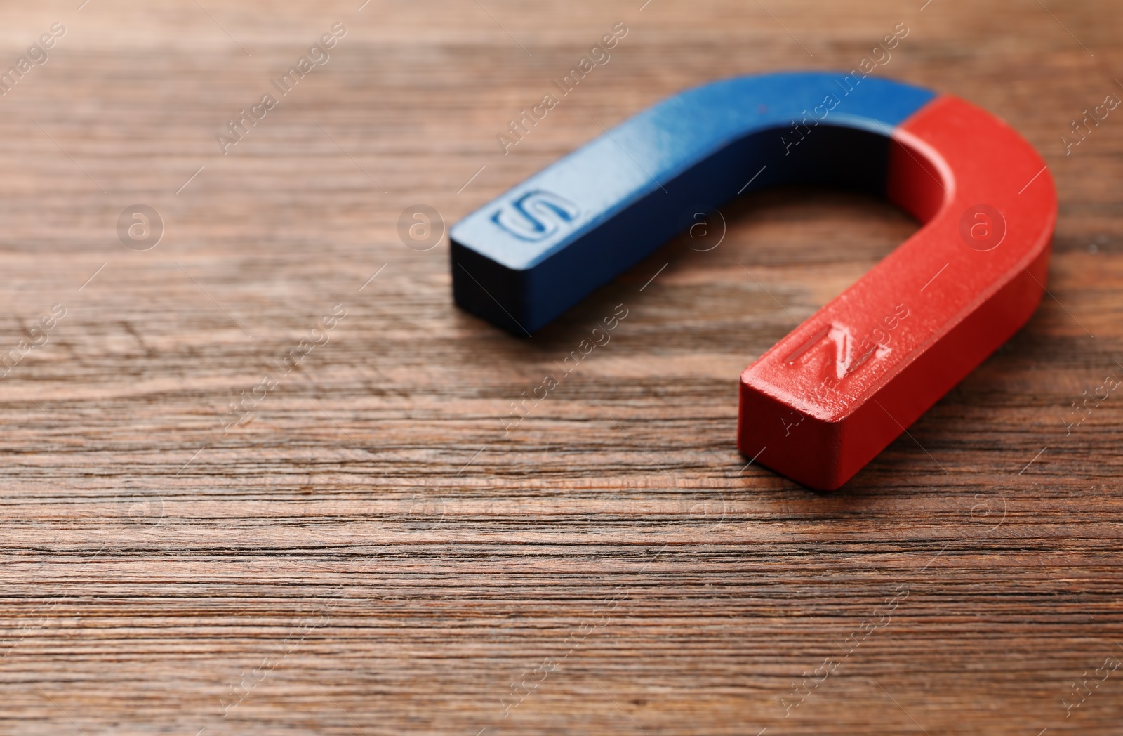 Photo of Red and blue horseshoe magnet on wooden background. Space for text