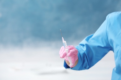 Doctor in medical glove with syringe on color background. Space for text