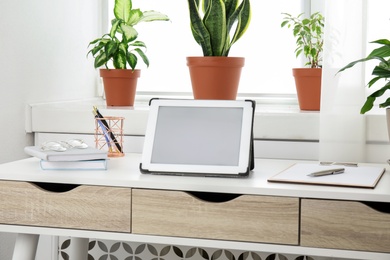 Photo of Tablet on table and houseplants in office interior, space for text