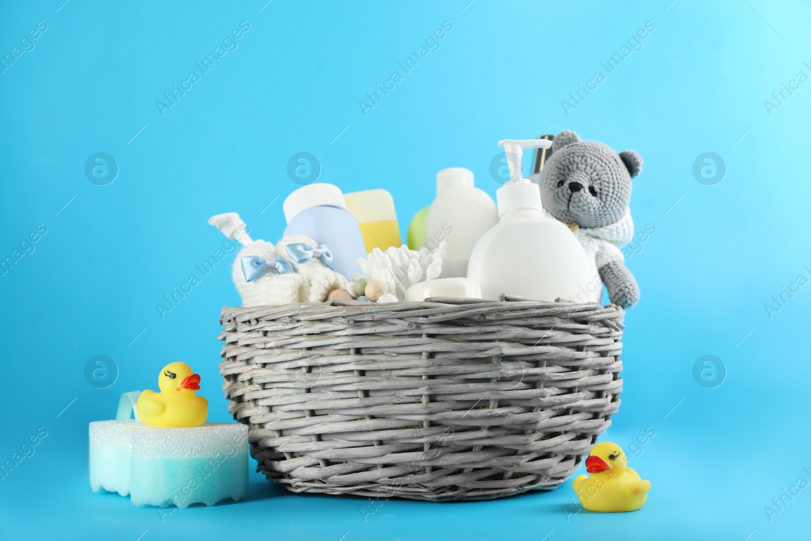 Photo of Wicker basket with different baby cosmetic products, bathing accessories and toys on light blue background
