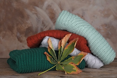 Photo of Stack of folded knitted sweaters and autumn leaf on wooden table against brown background