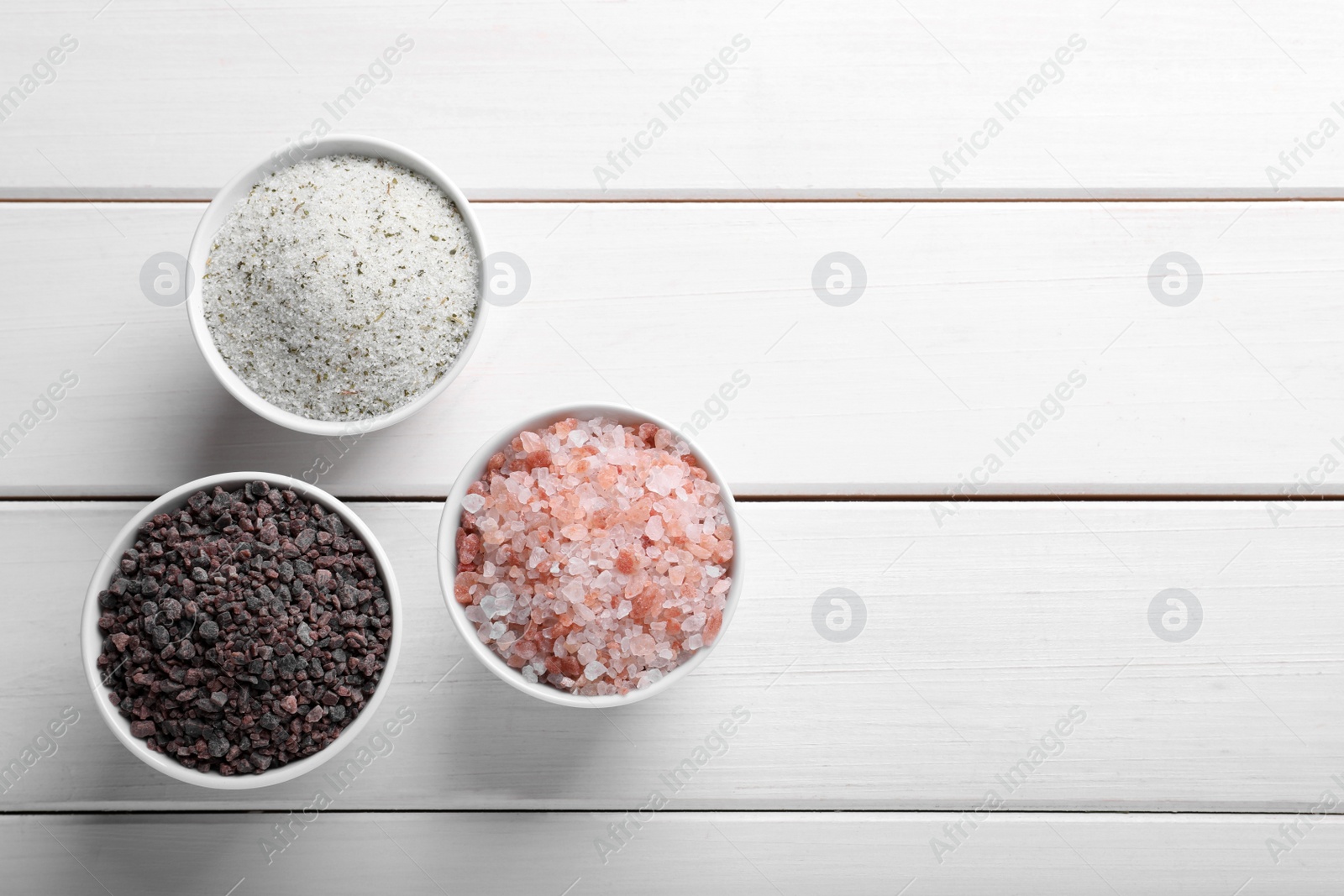 Photo of Different kinds of salt on white wooden table, flat lay. Space for text