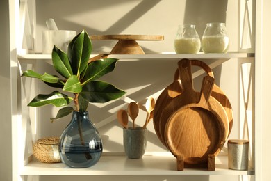 Wooden cutting boards, utensils, branch with green leaves and decor on shelving unit