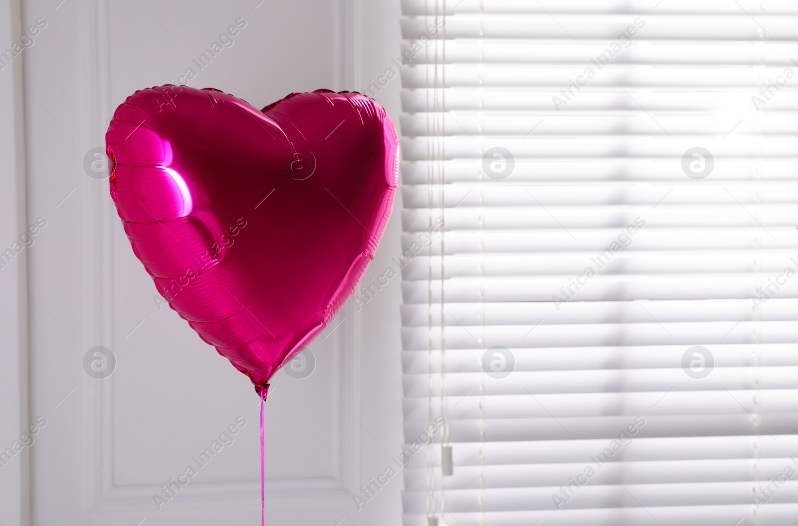 Photo of Festive heart shaped balloon in light room. Space for text