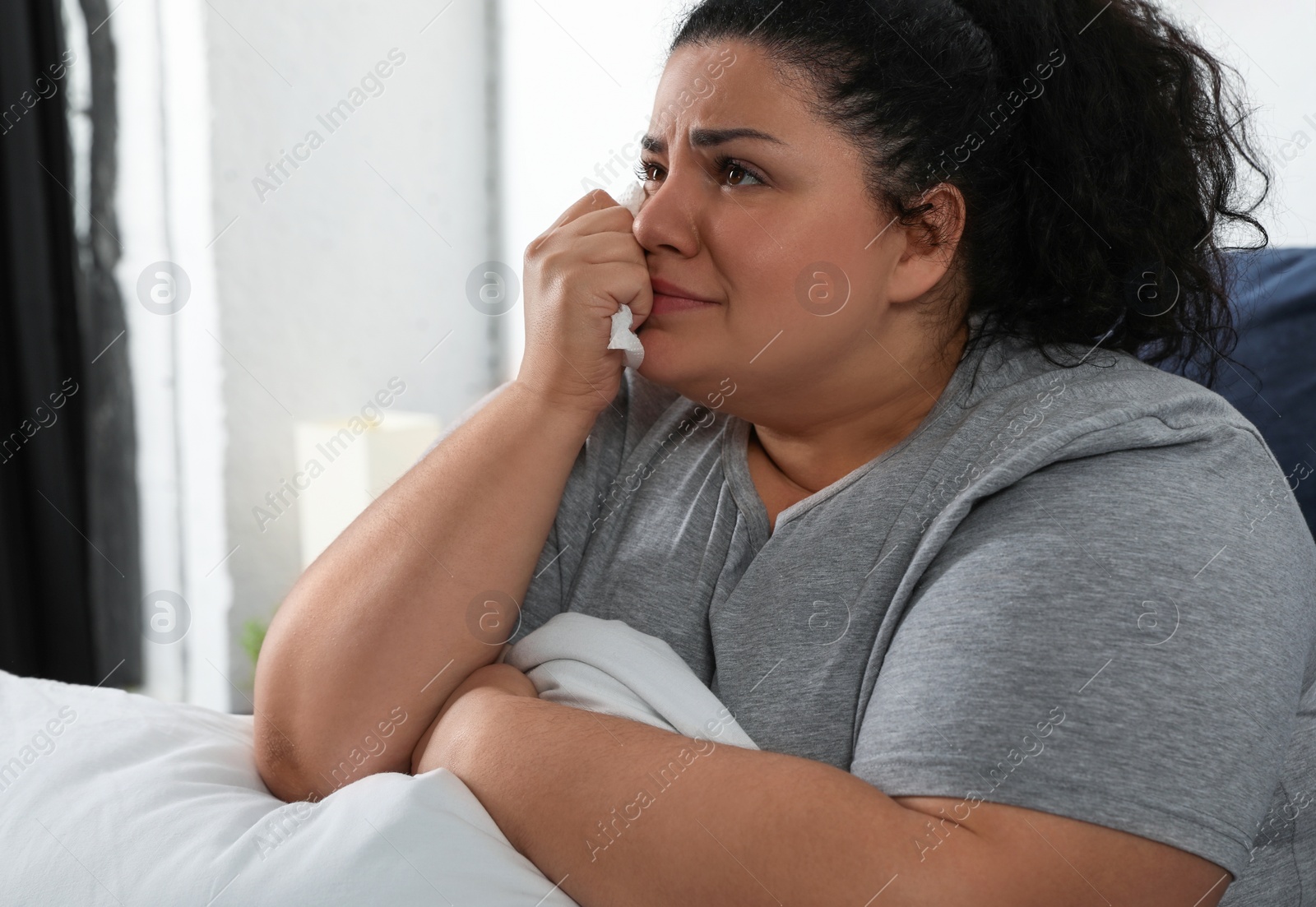 Photo of Depressed overweight woman crying while hugging pillow on bed