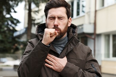 Photo of Sick man coughing on city street. Cold symptoms