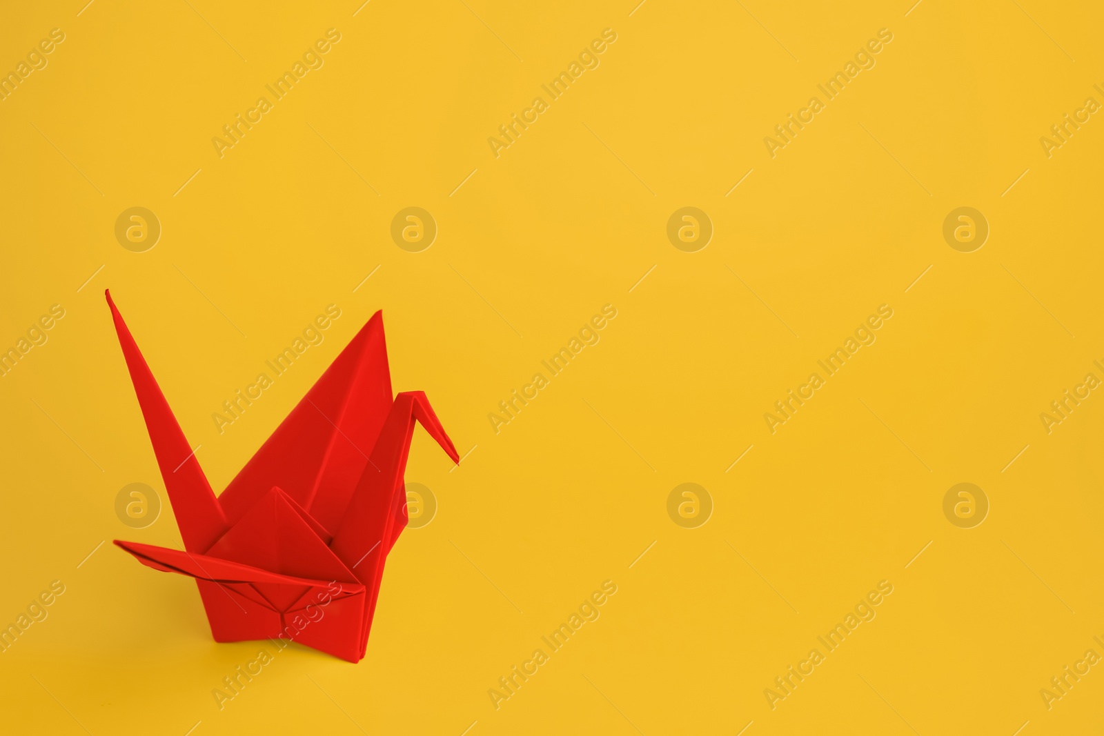 Photo of Origami art. Beautiful red paper crane on orange background, space for text