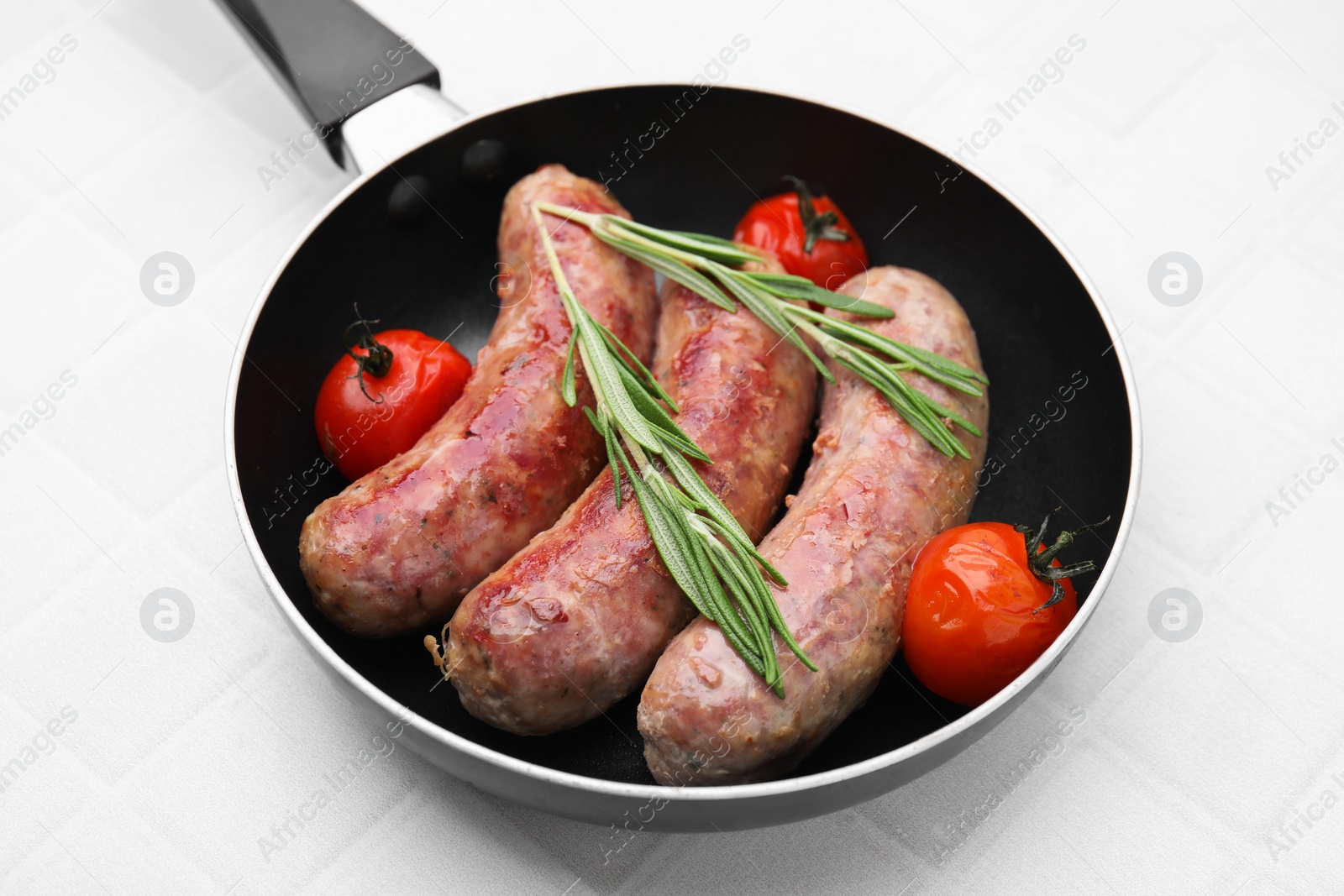 Photo of Frying pan with tasty homemade sausages, rosemary and tomatoes on white tiled table