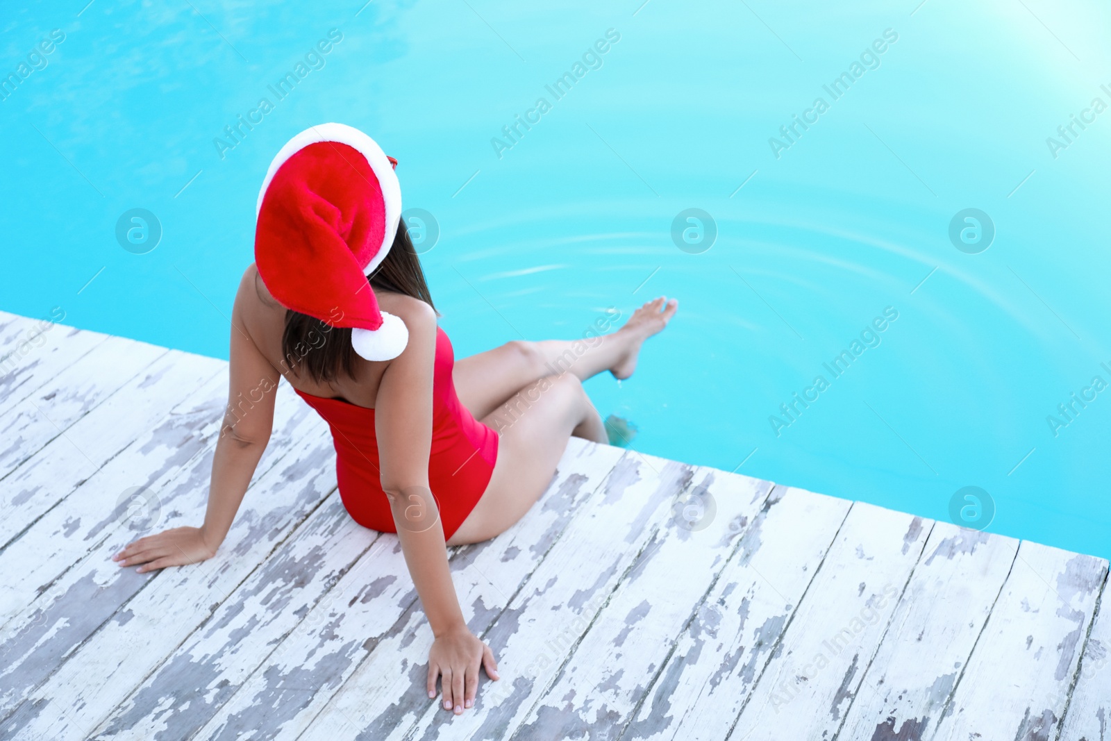 Photo of Young woman wearing Santa Claus hat near swimming pool, space for text. Christmas vacation