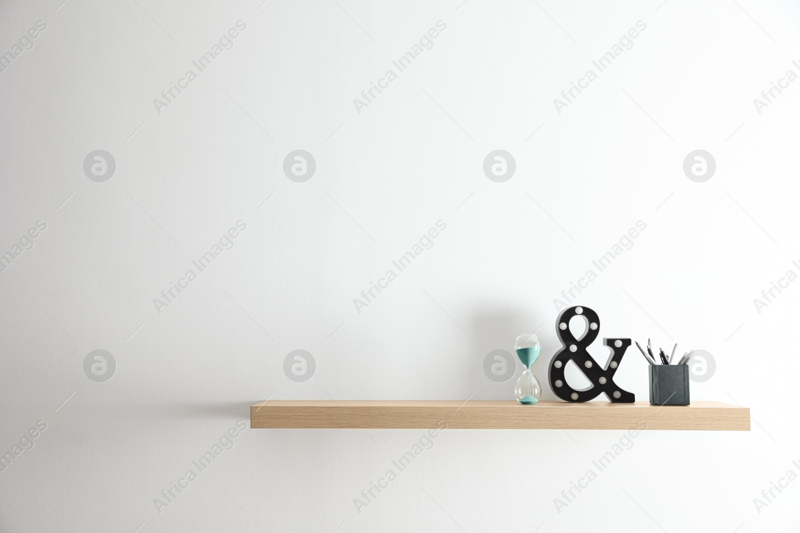 Photo of Wooden shelf with sand clock and stationery on light wall