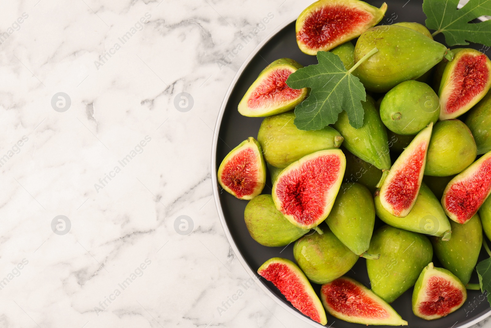 Photo of Cut and whole green figs on white marble table, top view. Space for text