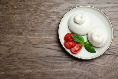 Photo of Delicious burrata cheese with basil and cut tomato on wooden table, top view. Space for text