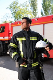 Portrait of firefighter in uniform with helmet near fire truck outdoors