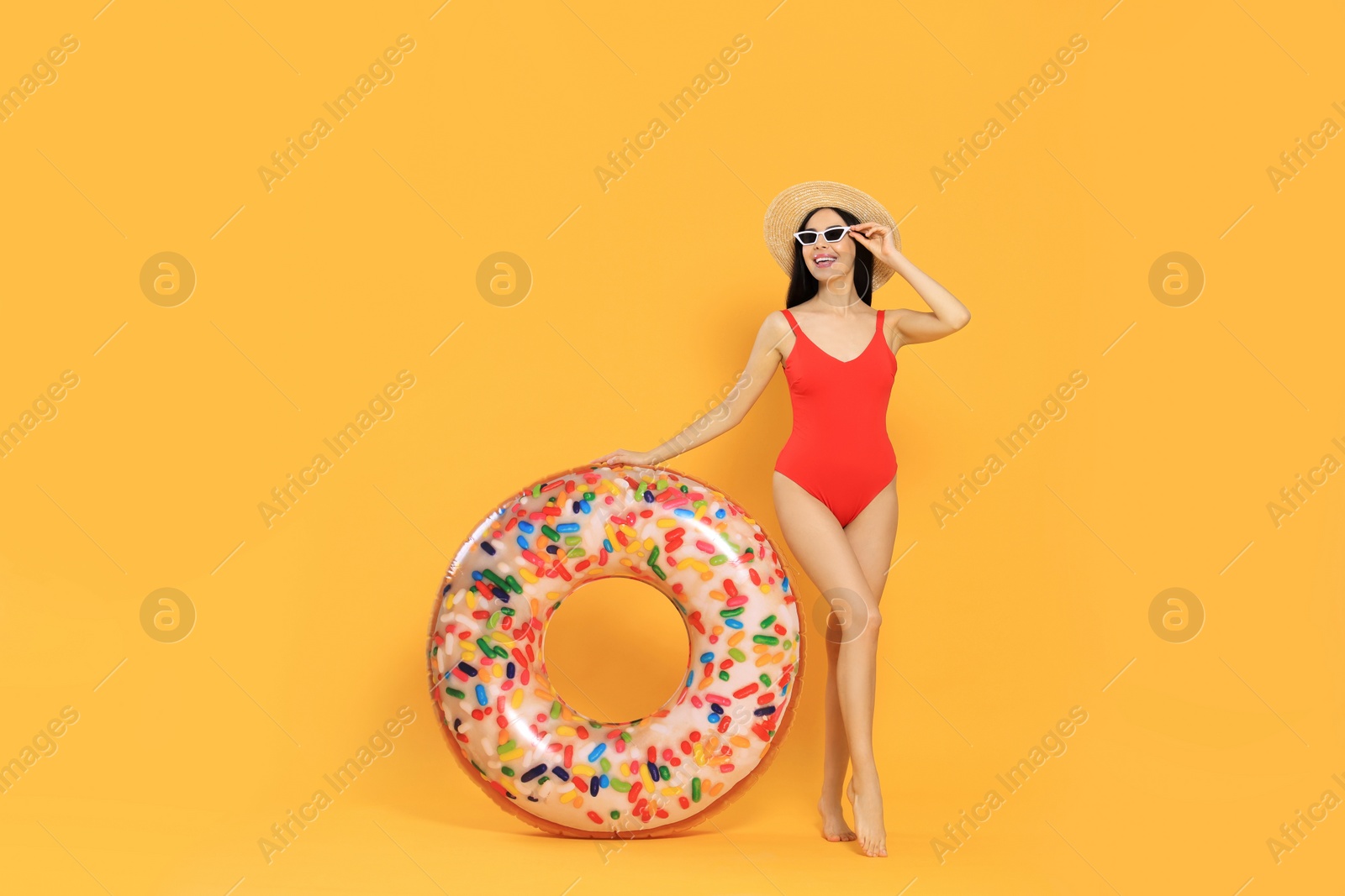 Photo of Happy young woman with beautiful suntan, hat, sunglasses and inflatable ring against orange background