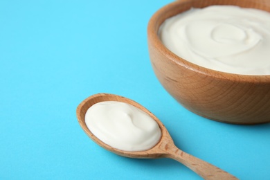 Wooden bowl and spoon of sour cream on light blue background