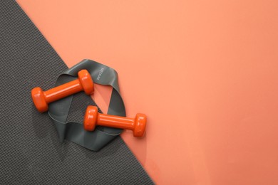 Photo of Dumbbells, yoga mat and fitness elastic band on coral background, flat lay. Space for text