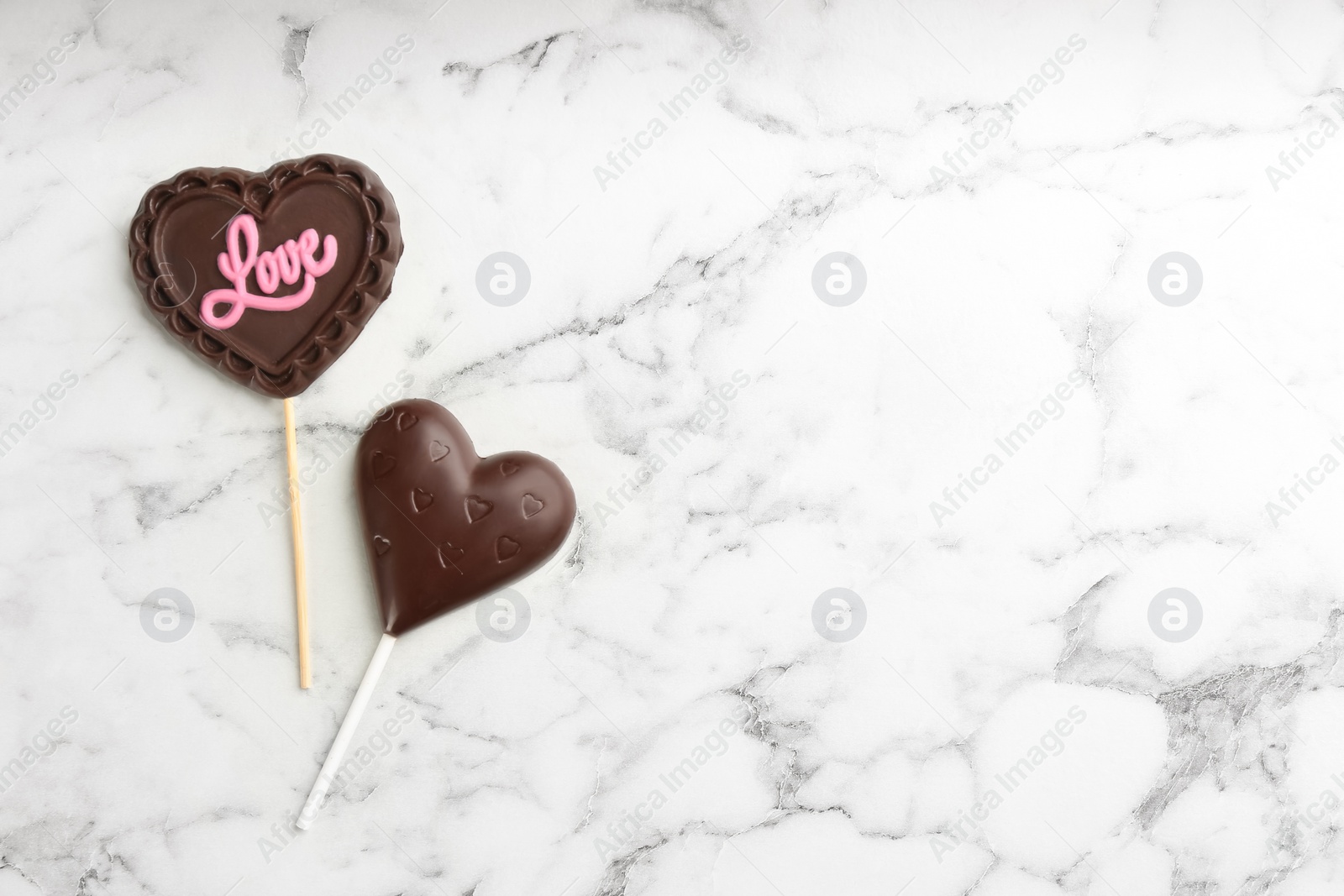 Photo of Different chocolate heart shaped lollipops on white marble table, flat lay. Space for text