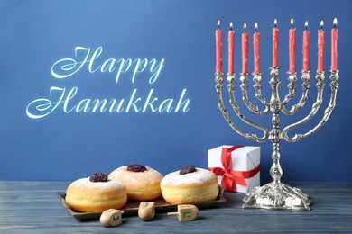 Image of Happy Hanukkah. Silver menorah, dreidels, gift box and sufganiyot on blue wooden table
