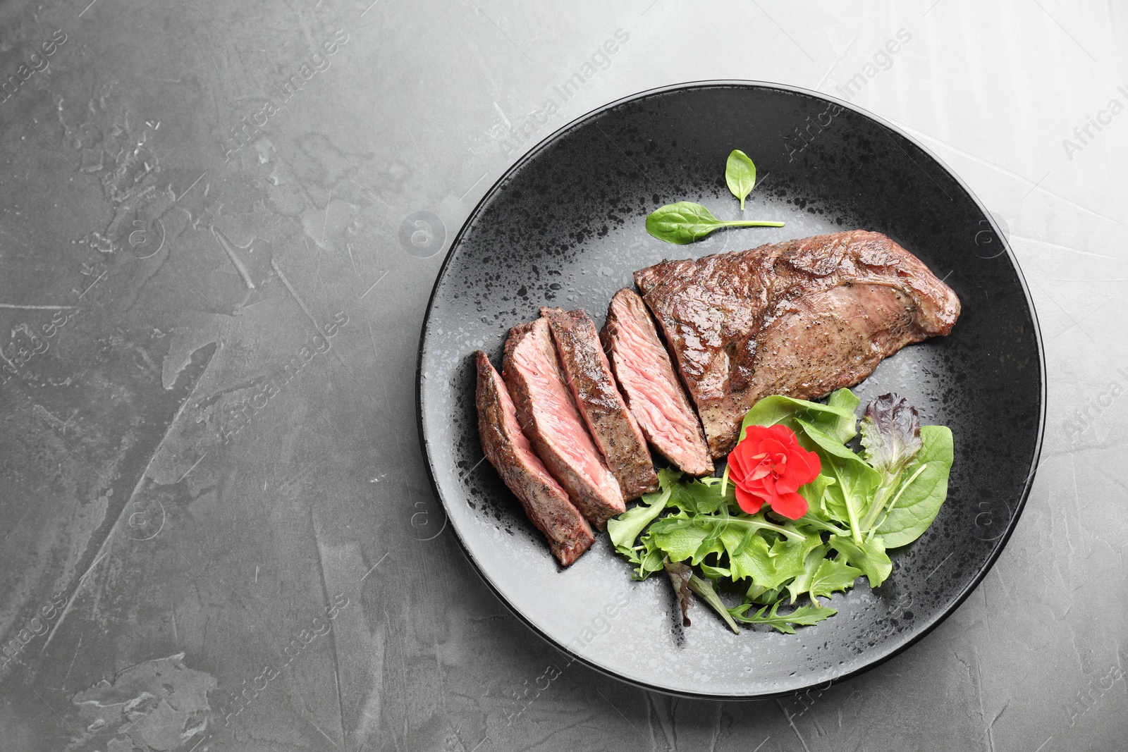 Photo of Pieces of delicious grilled beef meat and greens on grey table, top view. Space for text