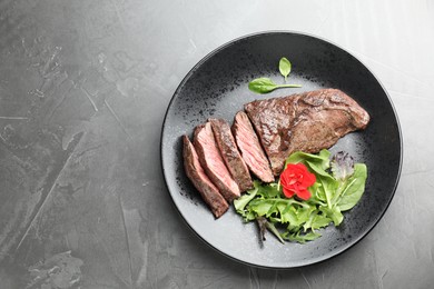 Photo of Pieces of delicious grilled beef meat and greens on grey table, top view. Space for text