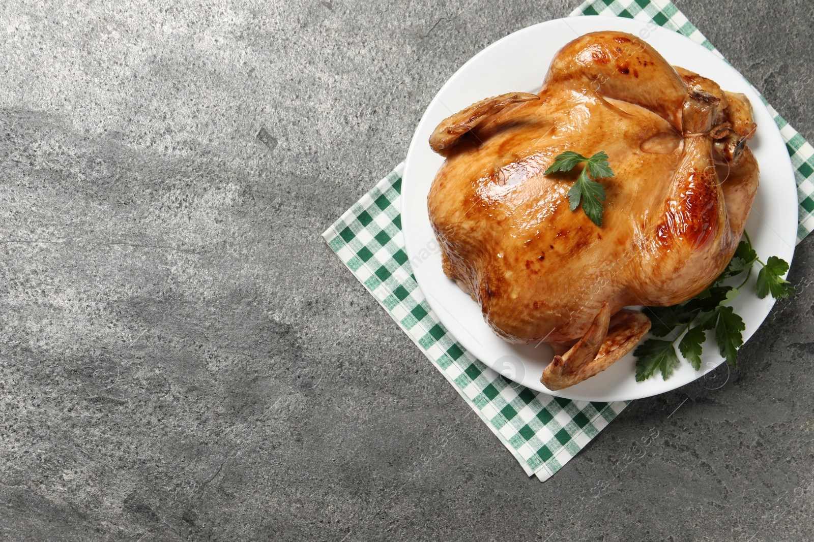 Photo of Tasty roasted chicken with parsley on grey textured table, top view. Space for text