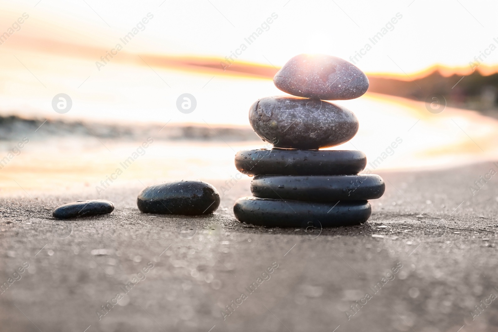 Photo of Dark stones on sand near sea at sunset, space for text. Zen concept