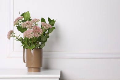 Stylish ceramic vase with beautiful flowers on table near white wall. Space for text
