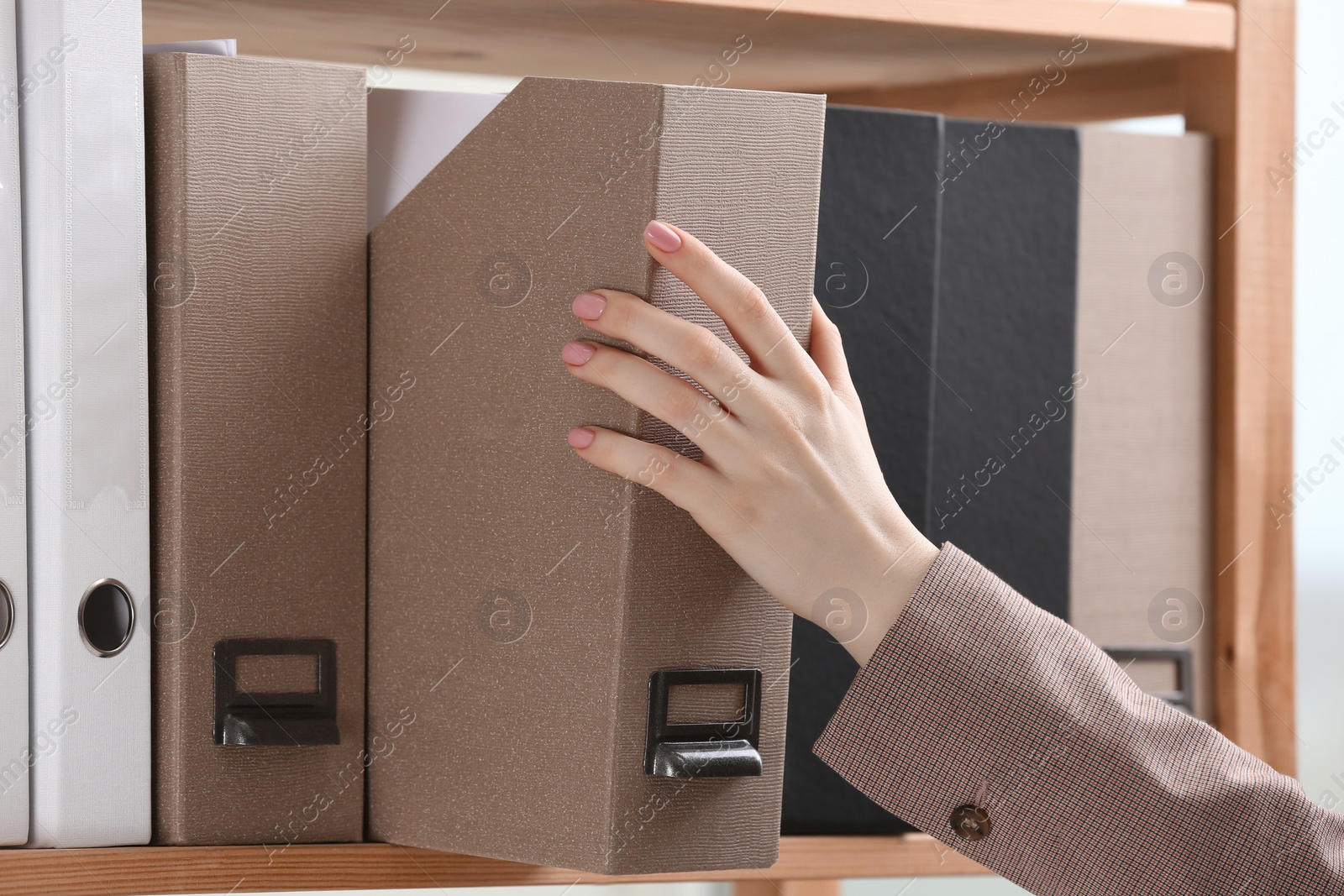 Photo of Woman taking folder with documents from shelf in office, closeup