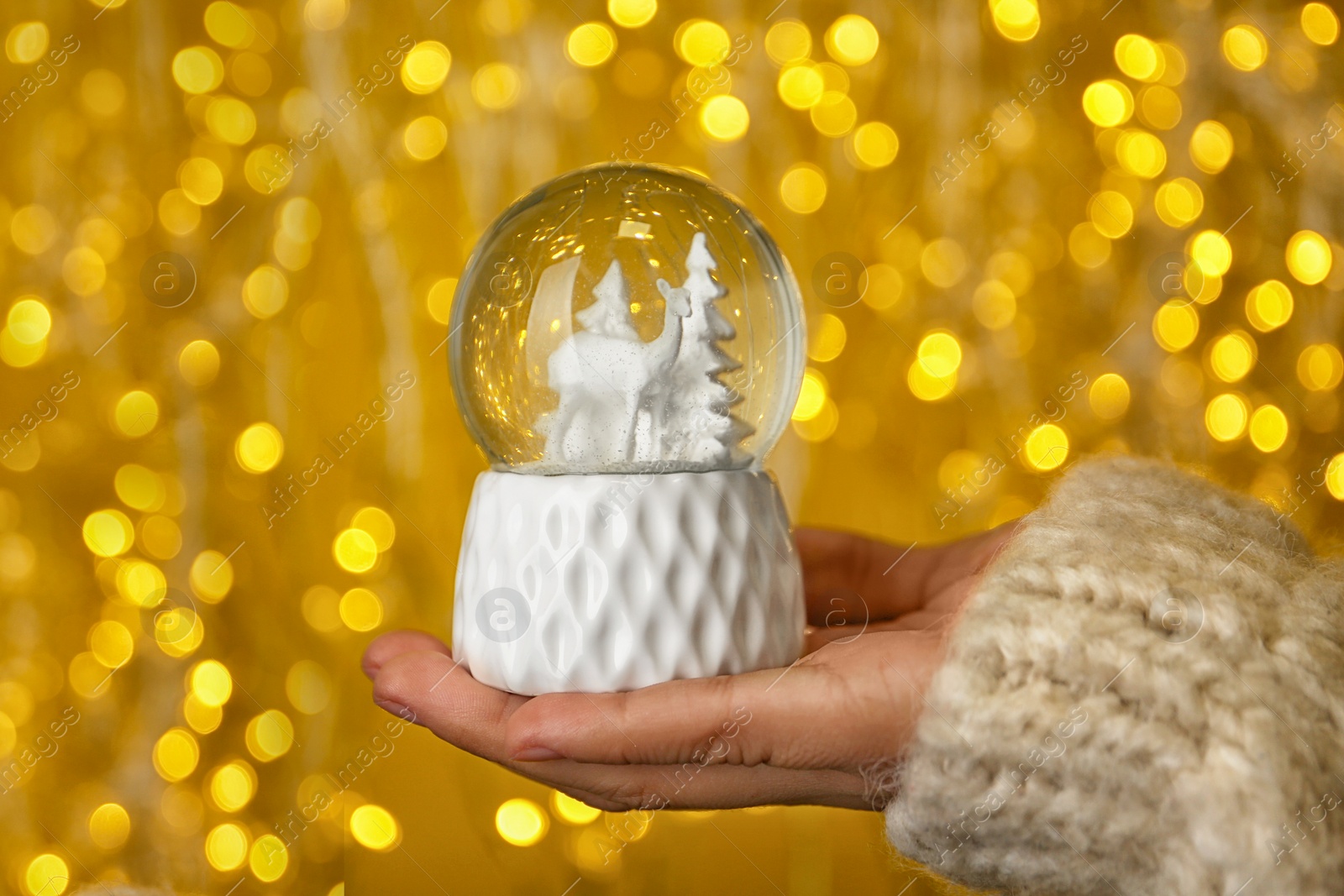 Photo of Woman holding snow globe with fir trees and deer against festive lights, closeup