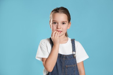 Photo of Cute little girl biting her nails on turquoise background