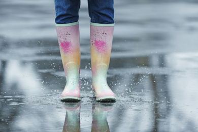 Photo of Woman in rubber boots walking outdoors on rainy day, closeup