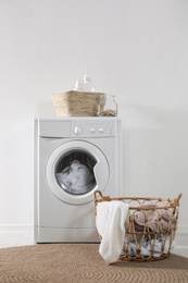 Photo of Modern washing machine and laundry baskets near white wall indoors. Bathroom interior