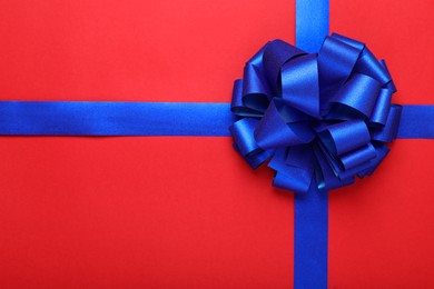 Photo of Blue ribbons with bow on red background, top view