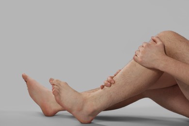 Photo of Man suffering from leg pain on grey background, closeup